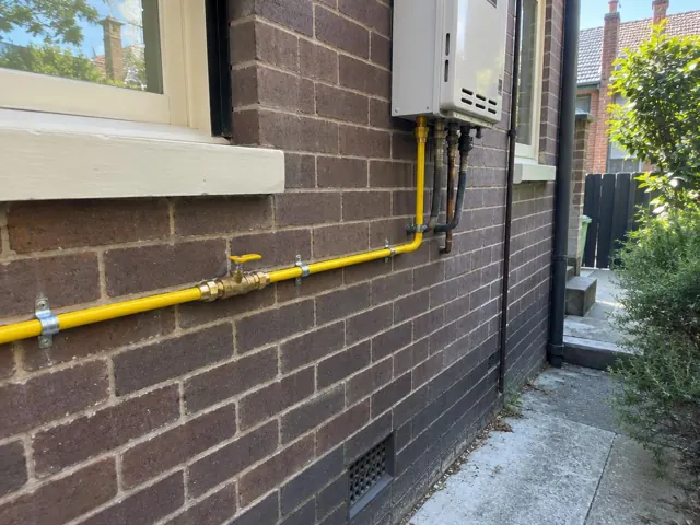 Yellow gas pipe and meter on a brick exterior wall beside a window in Woollahra