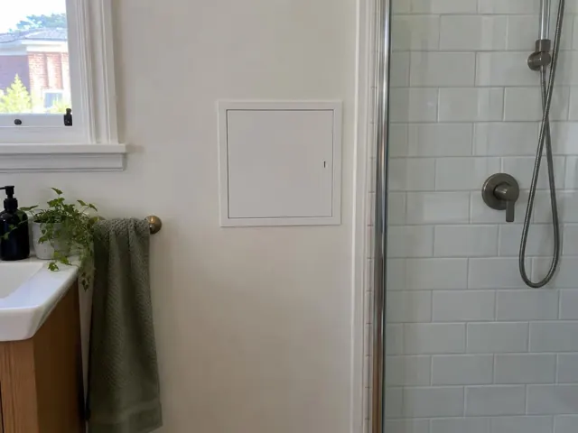Neat access panel on a painted bathroom wall beside a tiled shower in Double Bay